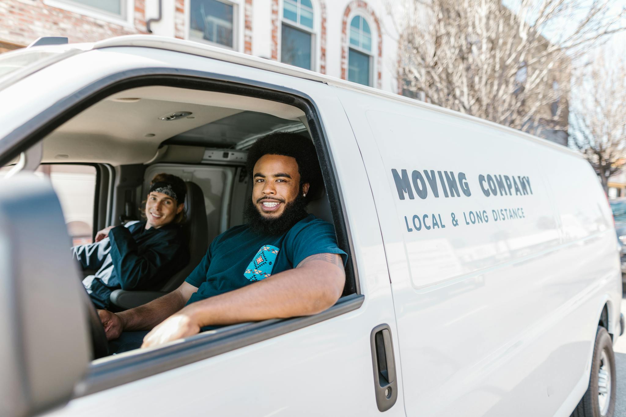 Two movers smiling from their moving company van parked on a sunny day.